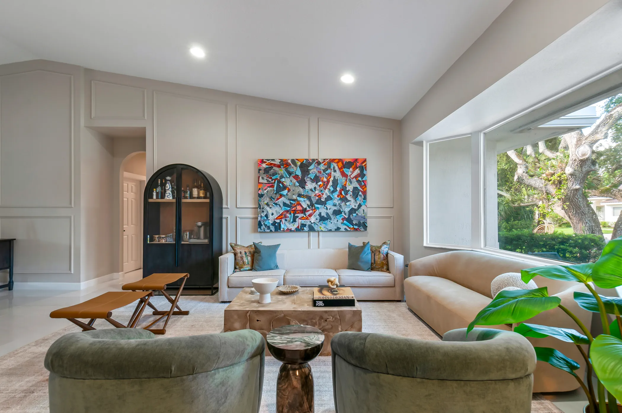 Living room with arched cabinet, green velvet chairs, and abstract art
