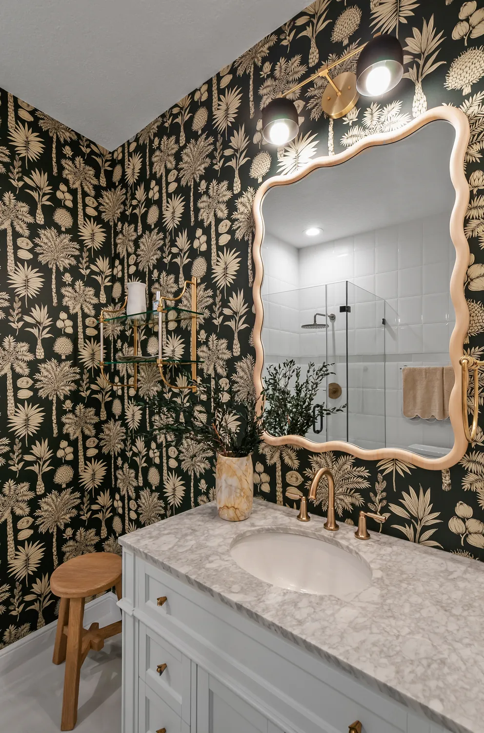 Powder bath with dark botanical wallpaper and scalloped mirror