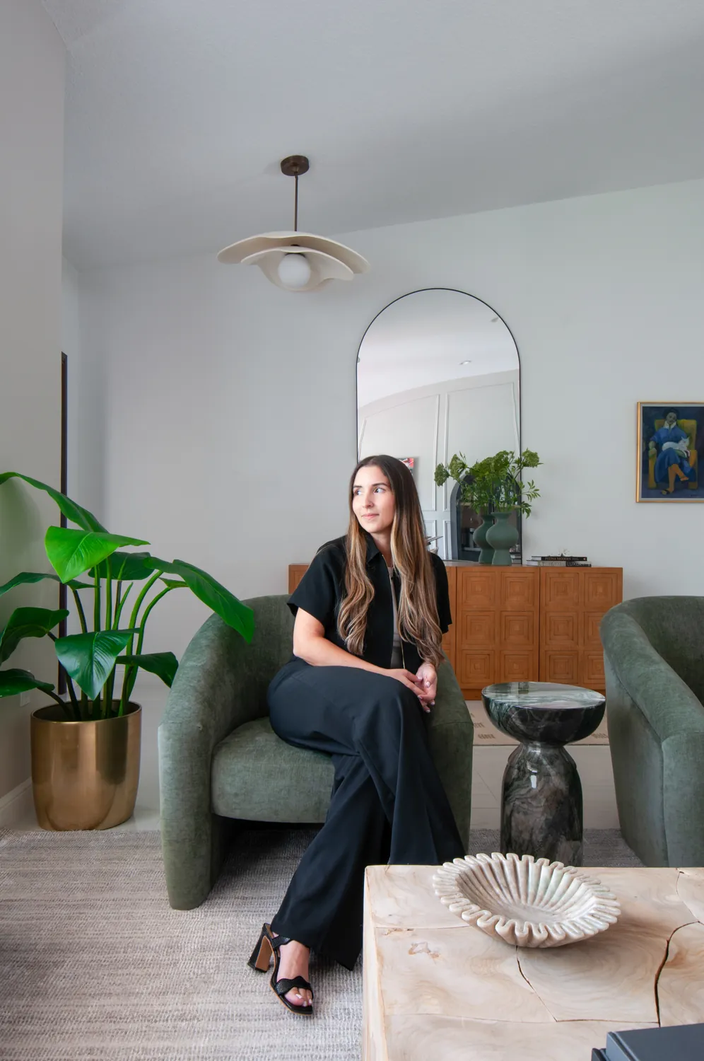 Camila seated in a green chair beside an arched mirror