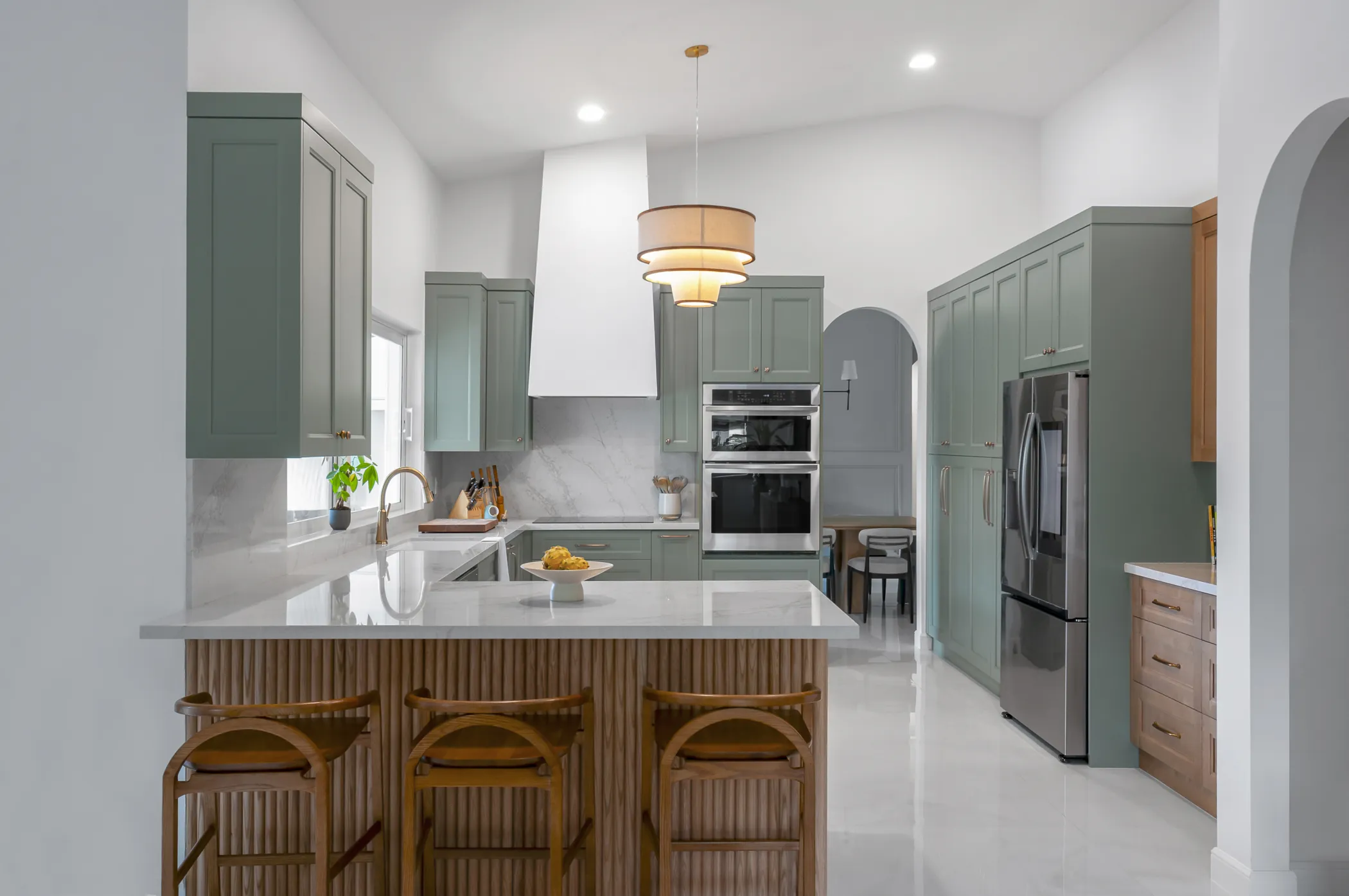 The kitchen, arched into the living space, with sage cabinetry on both runs