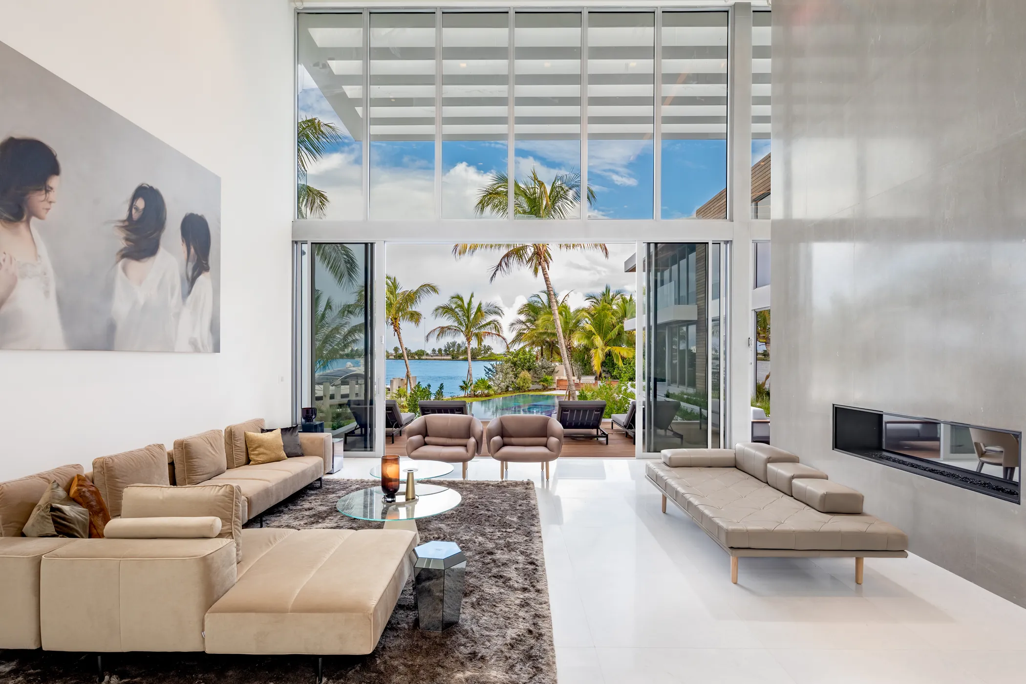 Double-height waterfront living room with concrete fireplace and palms beyond